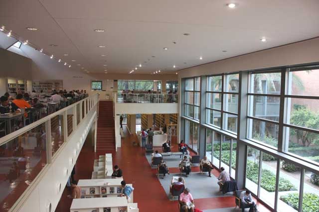 Interior moderno de la Biblioteca Infanta Elena, con amplios espacios de lectura. El diseño minimalista presenta estanterías llenas de libros y mesas de estudio en un ambiente luminoso.